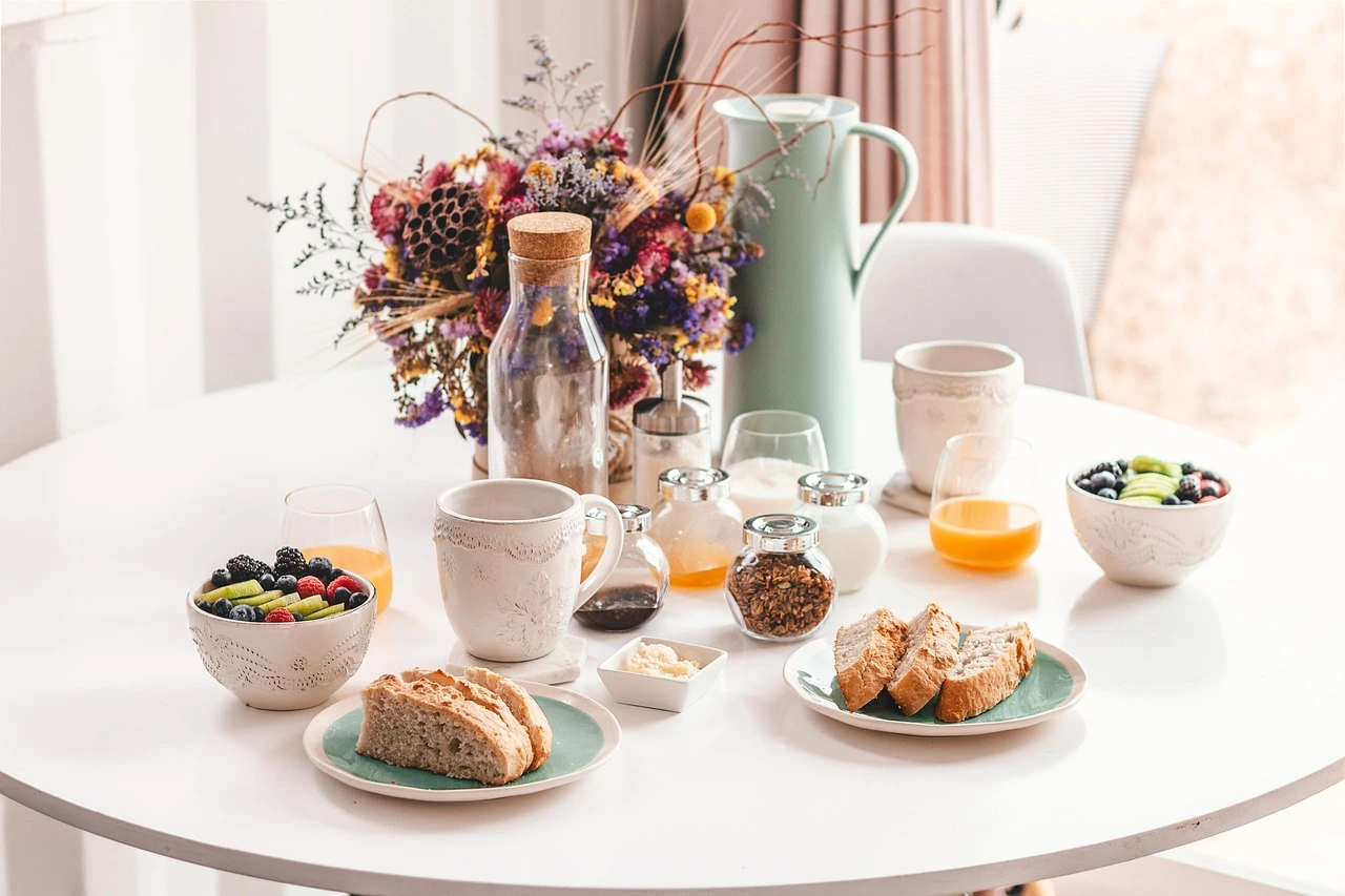 Gedeckter Frühstückstisch mit Saft, Obst, Brotscheiben, Kaffee und Dekoration