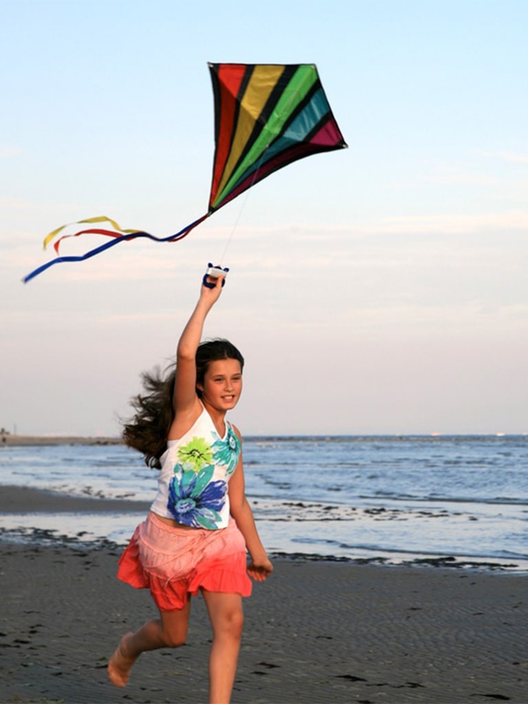 Kind spielt mit Drachen am Strand